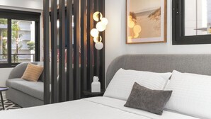 A hotel room with a bed, a gray sofa, a decorative wall panel, a bedside table with a tissue box, and a framed picture on the wall. - The Walk-Up Waikiki Beach  (Honolulu)