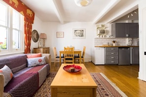 A cozy living room with a sofa, a dining table with chairs, and a kitchen area with cabinets and appliances.