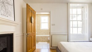 Een slaapkamer met een houten deur, een open haard, een groot raam en uitzicht op de badkamer.