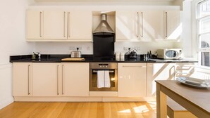 Een moderne keuken met lichte kastjes, een zwart aanrecht, roestvrijstalen apparatuur en een raam dat voor natuurlijk licht zorgt.