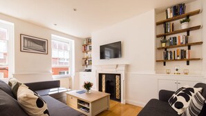 Een moderne woonkamer met een open haard, een televisie en boekenkasten.