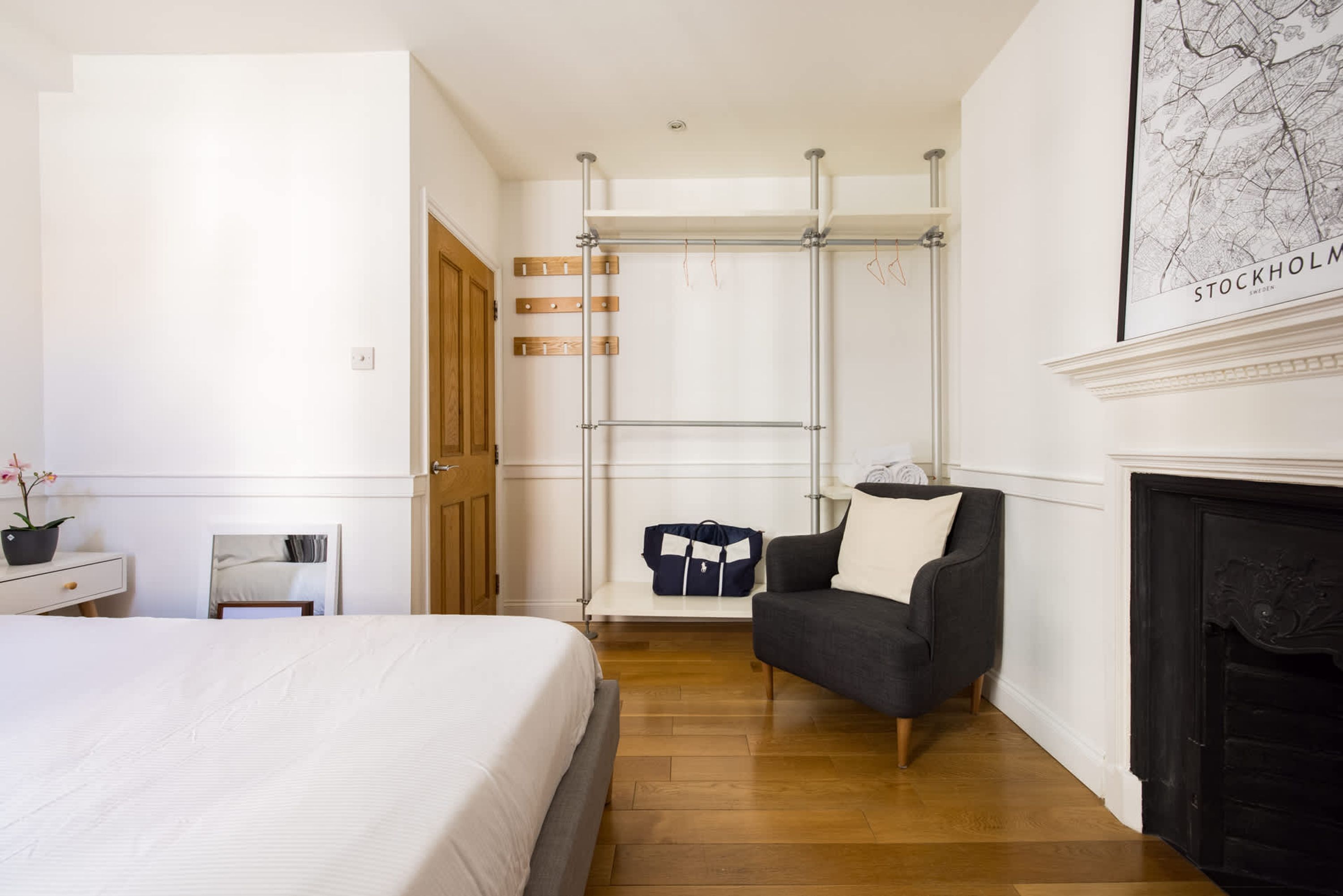 A bedroom with a bed, a chair, a sofa, a fireplace, and a wall-mounted drying rack.
