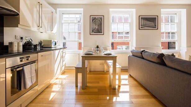 Een moderne keuken met een eettafel voor twee personen, een bank en grote ramen die voor veel natuurlijk licht zorgen.