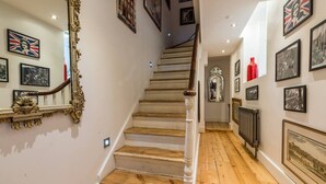 A staircase with wooden steps and white balusters, flanked by walls adorned with framed pictures and a red vase. - Spacious 4 Bed Apartment Opposite British Museum (London)