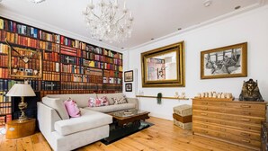 A living room with a large bookshelf, a sofa, a coffee table, a chandelier, and a wooden dresser. - Spacious 4 Bed Apartment Opposite British Museum (London)