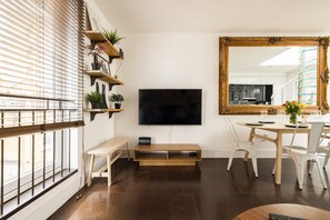 A modern living room with a flat-screen TV, wooden shelves with plants, a dining table with chairs, and a large mirror. - Stylish House Roof Garden Shoreditch (London)
