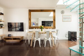A dining area with a wooden table, white chairs, a large mirror, a TV, and a glass staircase. - Stylish House Roof Garden Shoreditch (London)