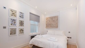 A bedroom with a bed, white walls, and artwork on the walls.