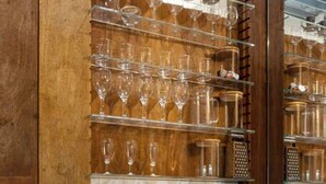A wooden bar area with shelves holding wine glasses and bottles, a fruit bowl, and a bottle of champagne.