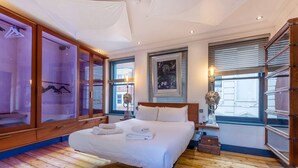 A bedroom with a large bed, wooden wardrobe, and a window with blinds.