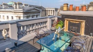 A rooftop terrace with a glass table and chairs, overlooking a cityscape.