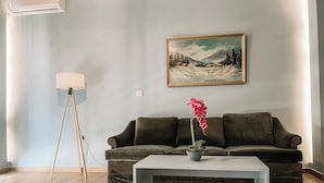Un soggiorno con un divano verde scuro, un tavolino da caffè bianco, un quadro raffigurante un paesaggio innevato e una lampada da terra.