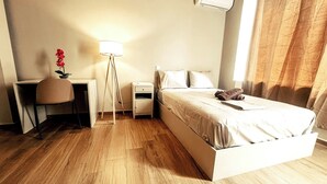 Una camera d'albergo con un letto, un comodino, una lampada, una scrivania, una sedia e un condizionatore d'aria.