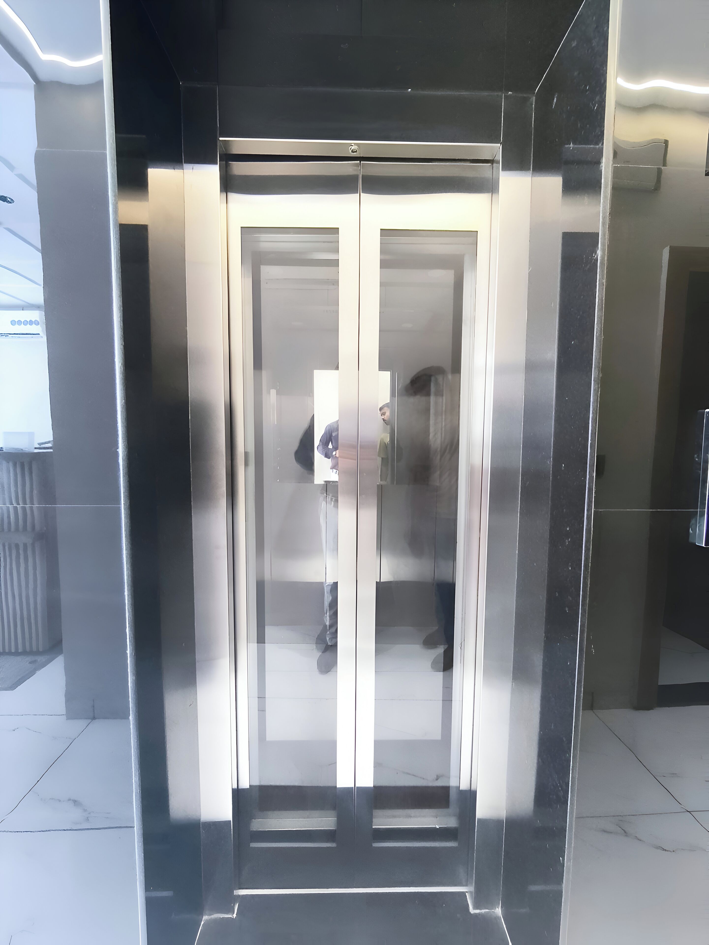 A modern elevator with a reflective glass door and metallic interior.