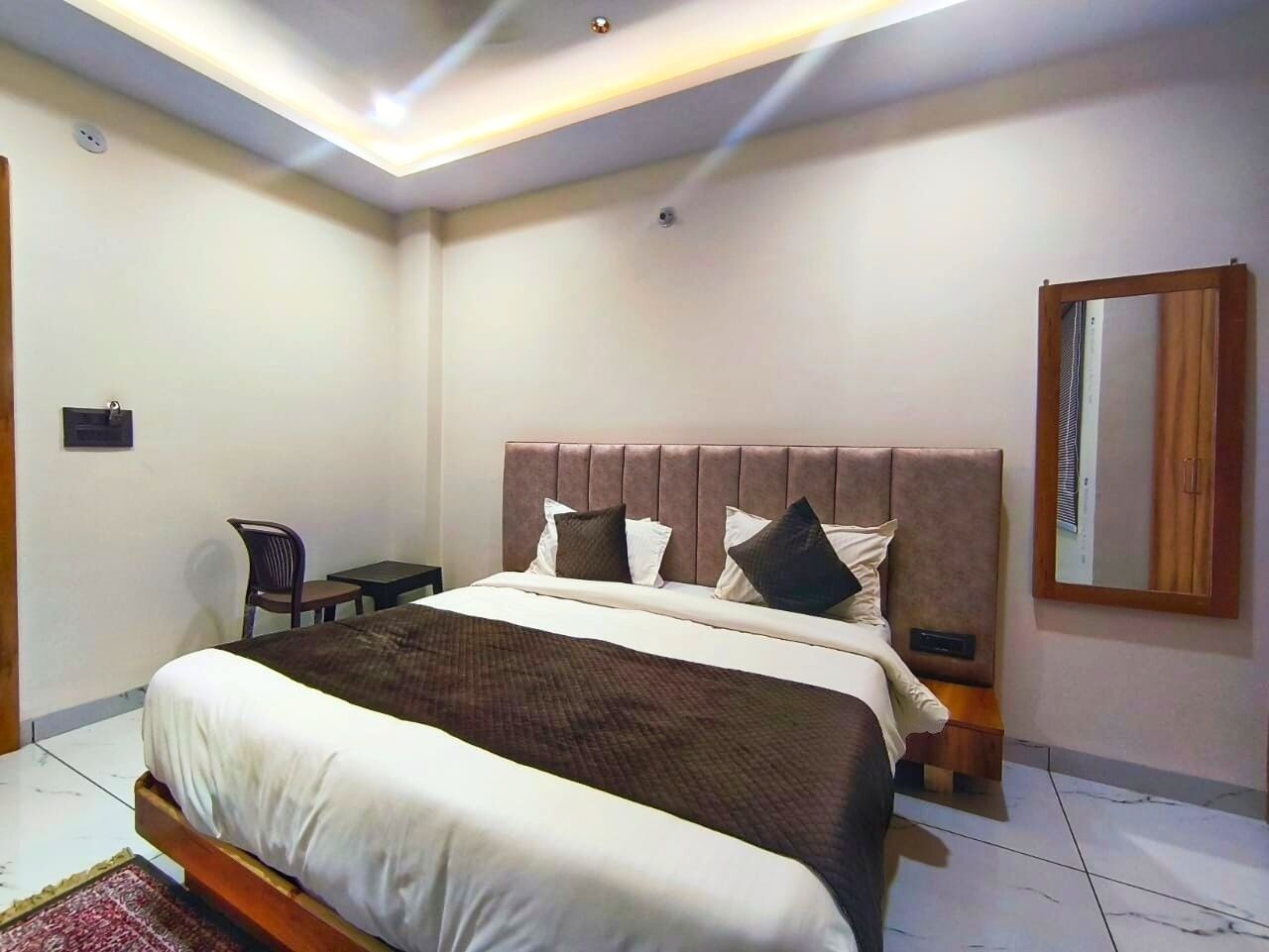 A bedroom with a large bed, a bedside table, a chair, and a mirror on the wall.