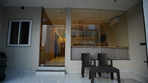 A modern interior with a glass door entrance, a small seating area with two chairs and a table, and a visible air conditioning unit.