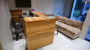 A compact living space with a wooden reception desk, a sofa, a desk chair, and a television mounted on the wall.