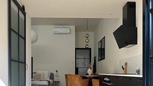 Eine moderne Küche mit schwarzen Schränken, ein Essbereich mit Holztisch und -stühlen sowie ein Wohnzimmer mit Sofa und Lampe.