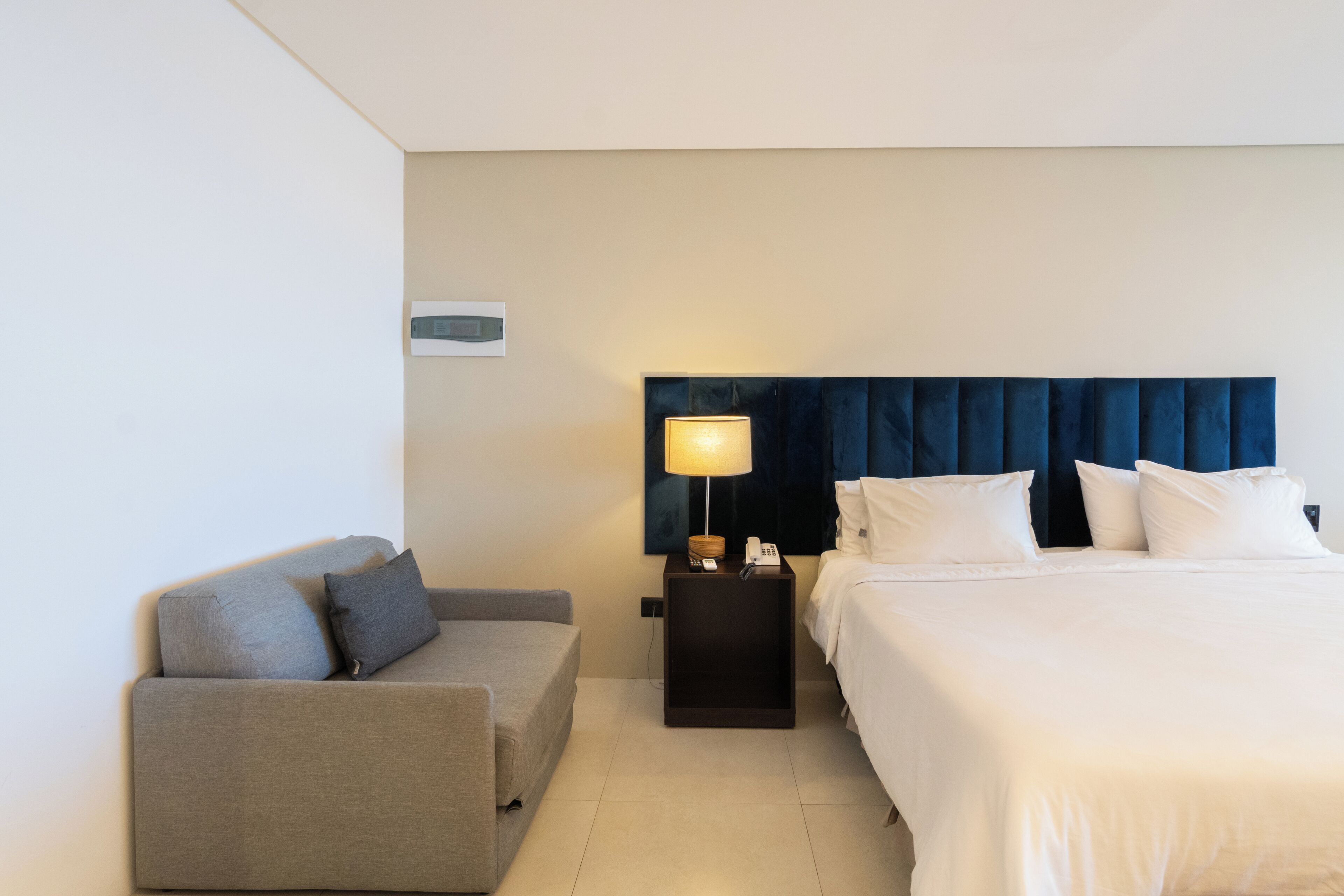 Habitación de hotel con cama, sofá, mesita de noche con lámpara y teléfono en la pared.