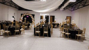 Een balzaal met meerdere ronde tafels, elk omringd door gouden stoelen.