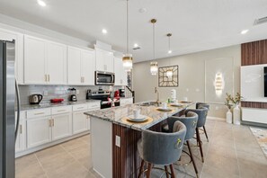 A modern kitchen with white cabinets, a central island with bar stools, stainless steel appliances, and pendant lighting.
