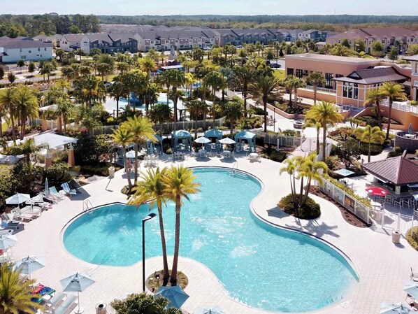 A resort with a large, curved swimming pool surrounded by palm trees and lounge chairs.