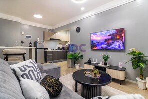 A modern living room with a grey sofa, a coffee table, and a TV displaying a sunset scene.