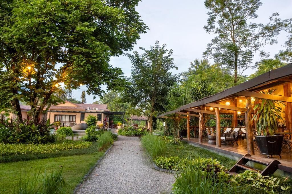 A garden pathway leading to a covered outdoor seating area with tables and chairs.