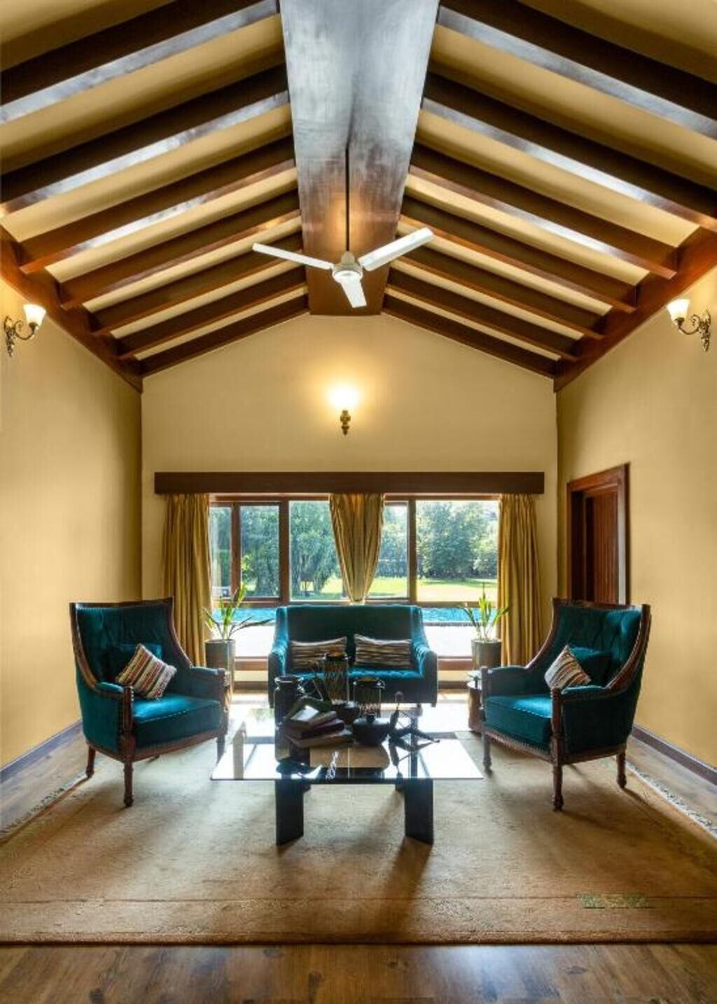A spacious room with a high ceiling, a ceiling fan, a large window with curtains, and two armchairs with a coffee table in the center.