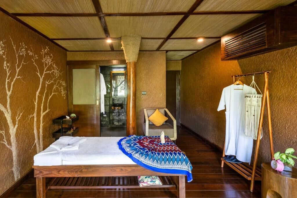 A room with a bed, a wooden bench, a clothing rack, and a wall with a tree design.