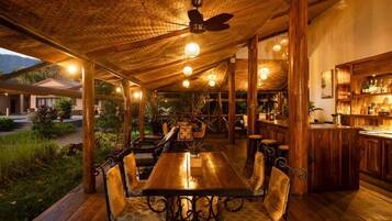 An outdoor dining area with wooden tables and chairs, a bar, and a ceiling fan.