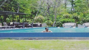A swimming pool with lounge chairs and a covered seating area, surrounded by lush greenery. - Nepal's First Boutique Spiritual Wellness and Golf Retreat Destination/2BR Villa (Devachuli)