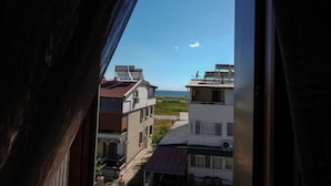 A view through a window of a building with a view of the sea and other buildings. - Akçay Otel Ege (Edremit)