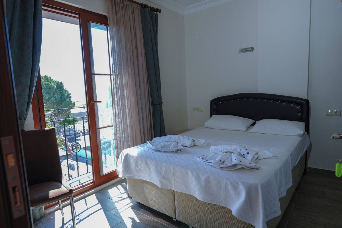 A hotel room with a bed, a chair, a balcony with a view, and a window with curtains.