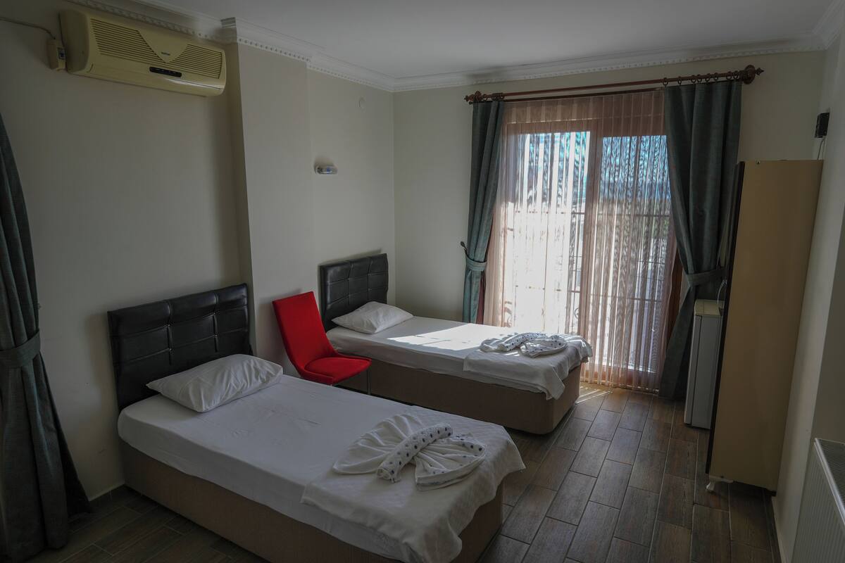 A hotel room with two single beds, a red chair, a wardrobe, and a radiator.