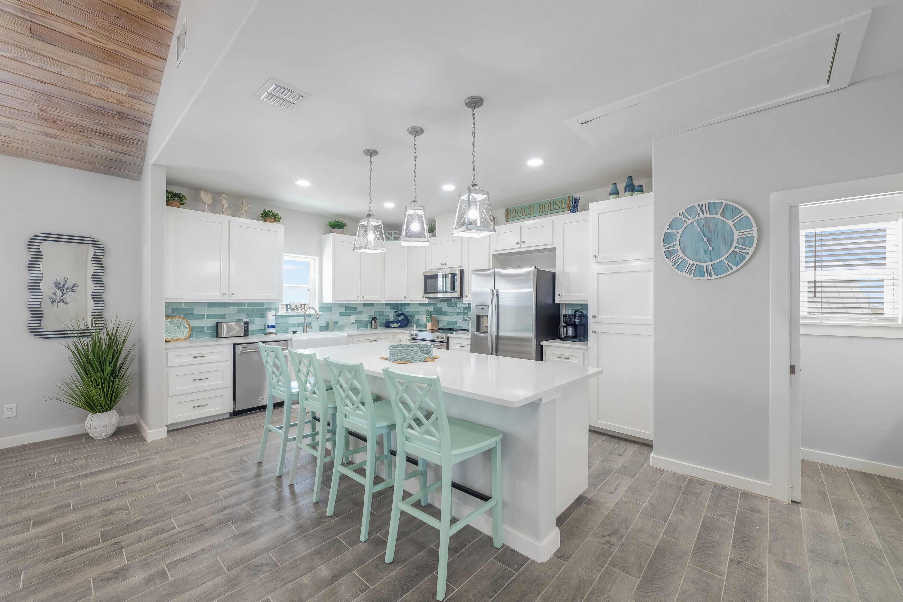 A modern kitchen with white cabinets, a large island with bar stools, pendant lighting, and a clock on the wall.