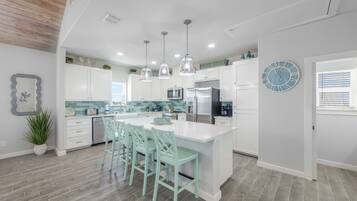 A modern kitchen with white cabinets, a large island with bar stools, pendant lighting, and a clock on the wall.