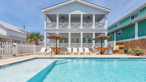 A two-story house with a pool, white railings, and a wooden deck with lounge chairs and umbrellas. - Spacious upscale home, community pool, private hot tub, close to the beach! (Port Aransas)