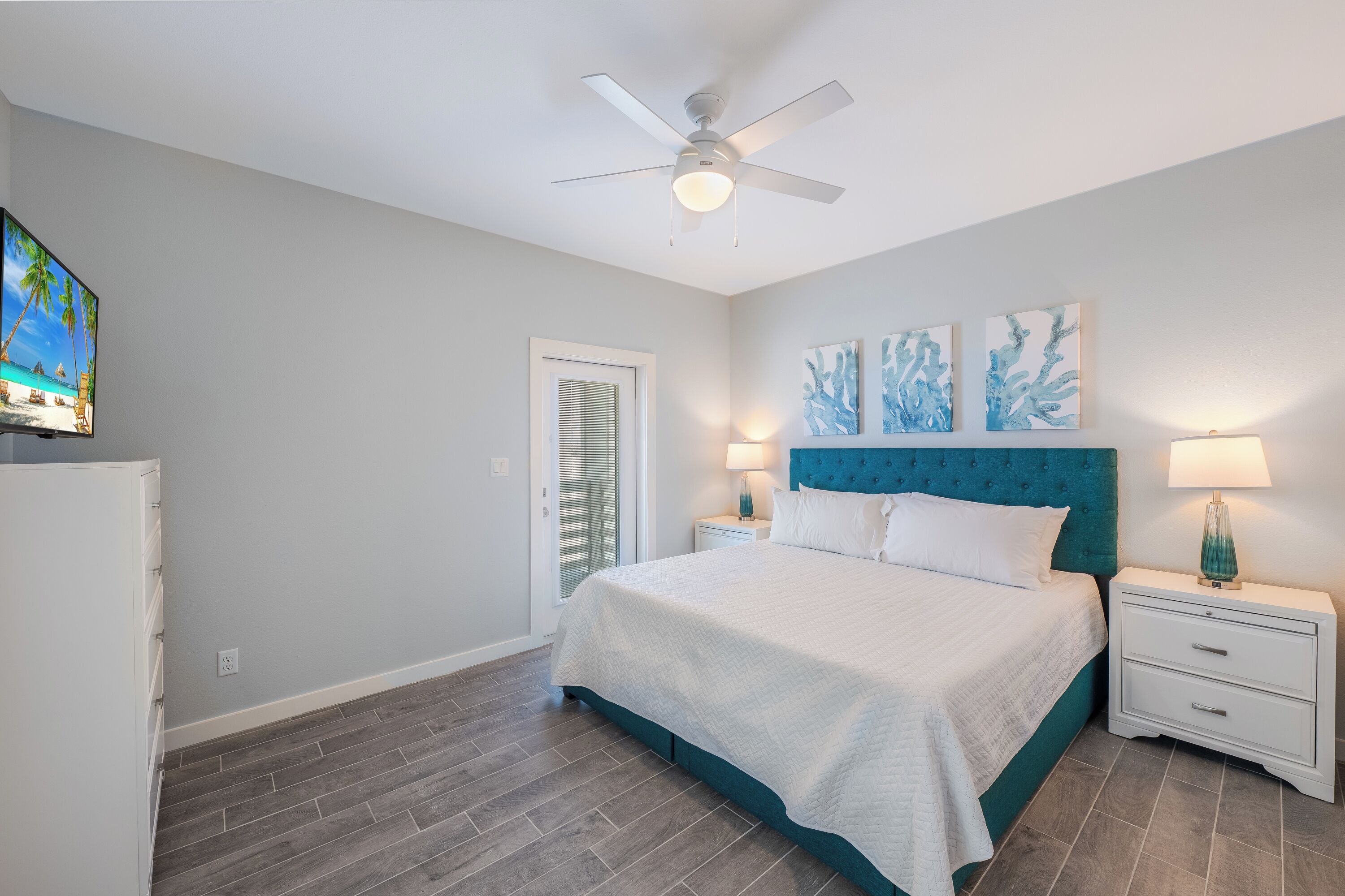 A bedroom with a bed, nightstands, a ceiling fan, artwork, and a television.