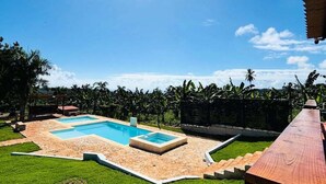 A swimming pool with a sunlit sky and lush greenery.