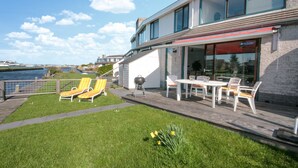 Une terrasse extérieure moderne avec vue sur l’eau, comprenant un barbecue, des chaises longues et une table à manger.