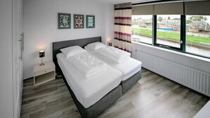 Une chambre moderne avec deux lits, une table de chevet avec une lampe et une fenêtre donnant sur un canal et des immeubles.