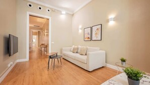 A modern living room with a sofa, a coffee table, a TV mounted on the wall, and a hallway leading to another room. - Sweett | Sepulveda 2C (Barcelona)