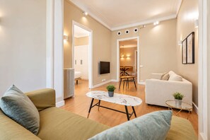 A modern living room with a sofa, a coffee table, and a TV. There is a dining area with a table and chairs.
