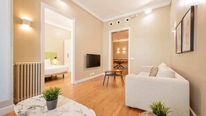 A modern living room with a sofa, a TV mounted on the wall, a dining area with a table and chairs, and a radiator. - Sweett | Sepulveda 2C (Barcelona)