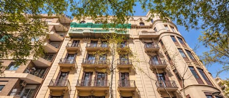 A multi-story building with balconies, a green awning, and a clear blue sky.