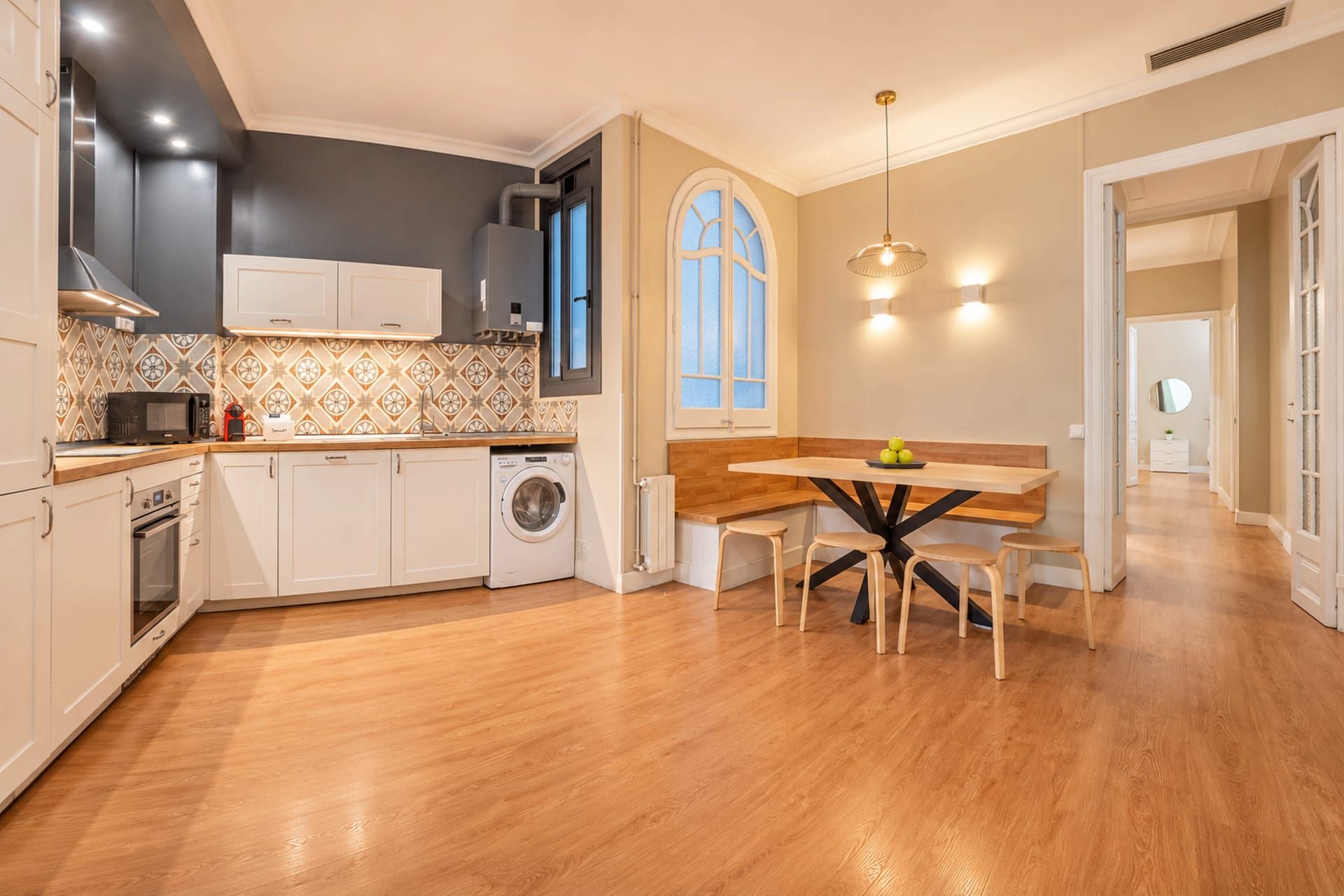 A modern kitchen with built-in appliances, a dining area with a wooden table and stools, and a large window with a view.