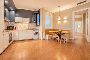 Cozinha moderna com eletrodomésticos embutidos, sala de jantar com mesa e banquetas de madeira, e uma janela grande com vista.