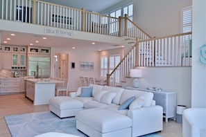 A spacious living area with a large sectional sofa, a kitchen with white cabinets, and a staircase leading to an upper level.