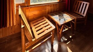 A wooden cabin with a large window overlooking a mountainous landscape. Inside, there is a wooden bench and a small table. - Manali Mornings (Manali)